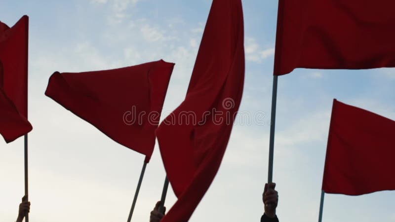 Χέρια των κυματίζοντας κόκκινων σημαιών ομάδων ανθρώπων ενάντια στο μπλε ουρανό
